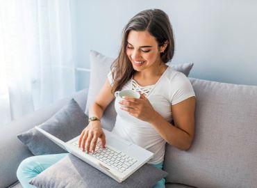 Woman drinking coffee while looking at laptop