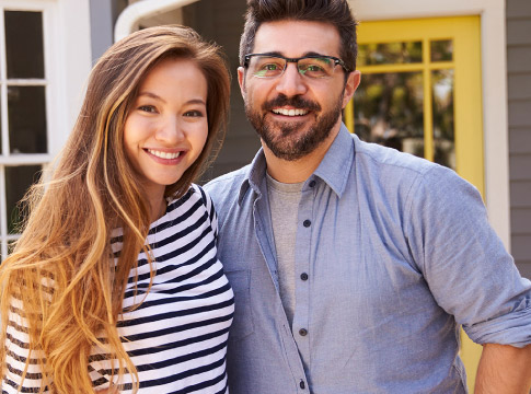 Happy young couple stand outside their home.