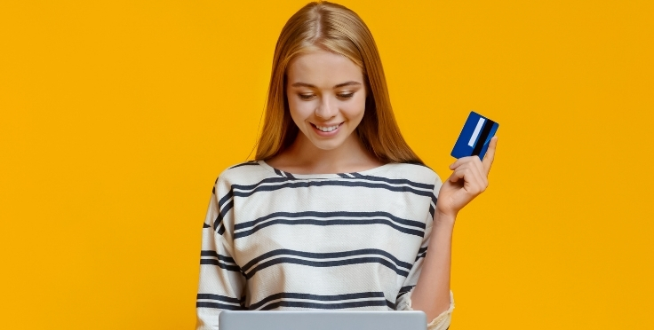 Teen on laptop smiling and holding a credit card