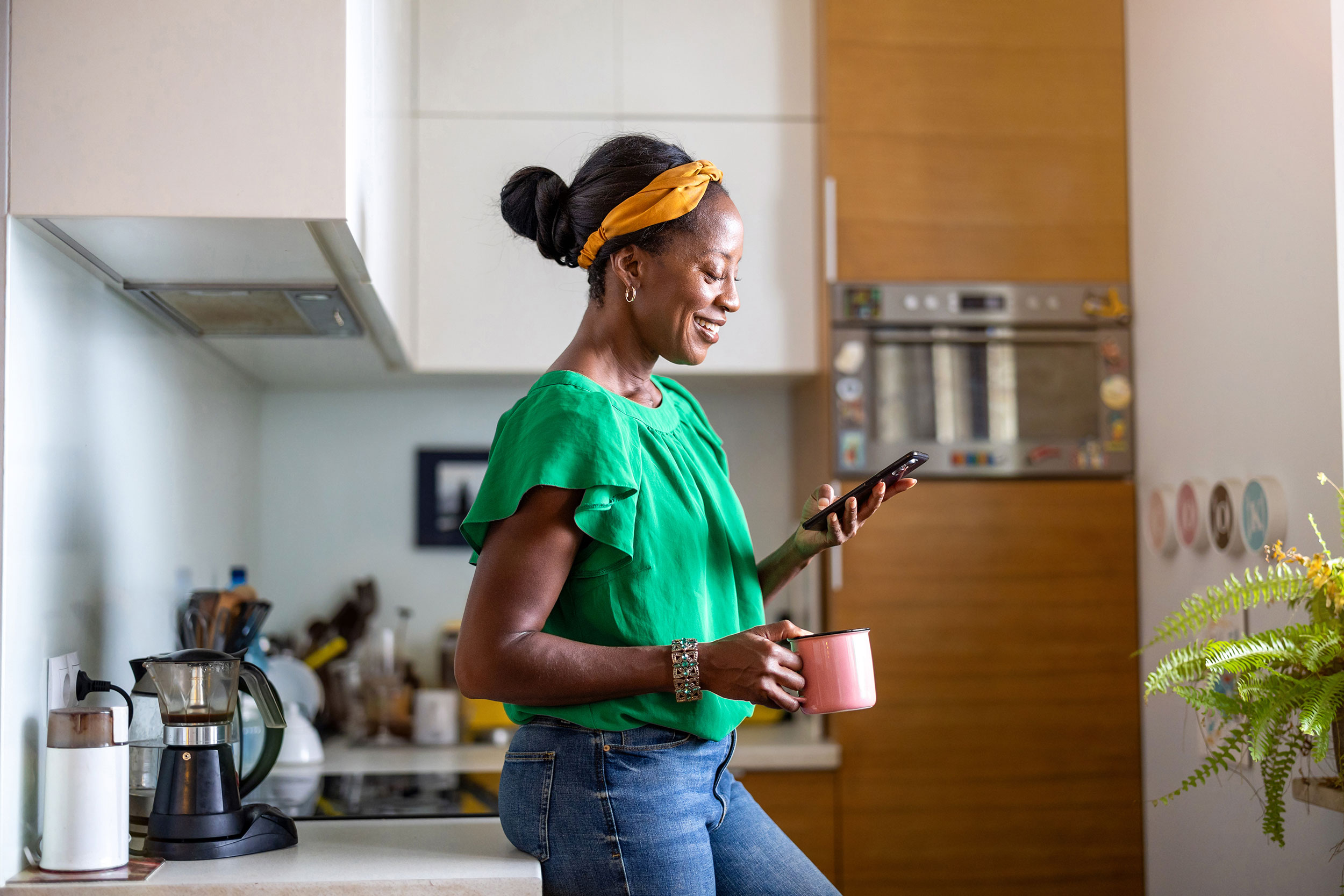 Woman standing in kitchen holding a mug and using her phone